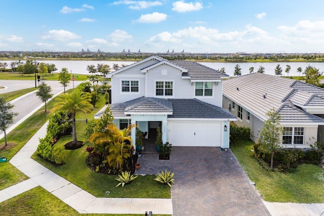 traditional home with decorative driveway, an attached garage, a water view, and a tile roof