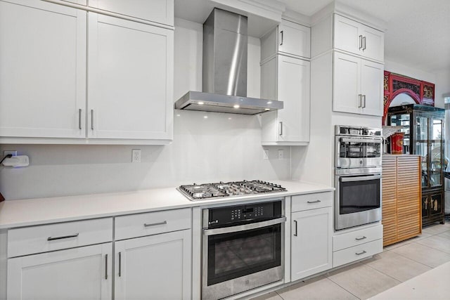 kitchen featuring white cabinets, appliances with stainless steel finishes, light countertops, wall chimney exhaust hood, and light tile patterned floors