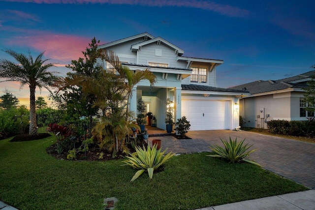 traditional-style home featuring an attached garage, decorative driveway, stucco siding, and a yard