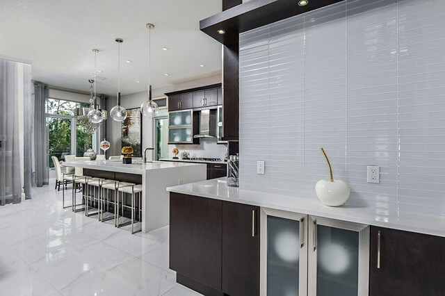 kitchen featuring decorative backsplash, an island with sink, a breakfast bar area, light countertops, and hanging light fixtures