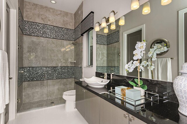 full bathroom featuring double vanity, a sink, toilet, and tiled shower