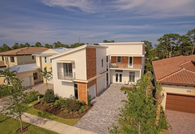 modern home with a garage, a balcony, decorative driveway, stucco siding, and french doors