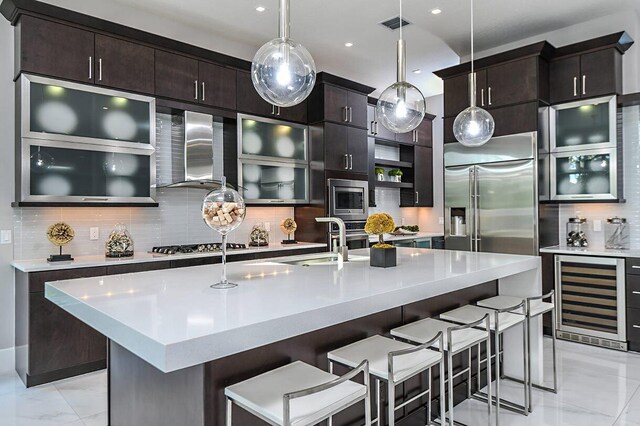 kitchen with wall chimney range hood, decorative backsplash, a sink, wine cooler, and built in appliances