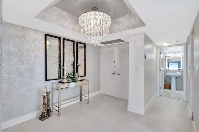 hall featuring visible vents, a sink, baseboards, an inviting chandelier, and a tray ceiling