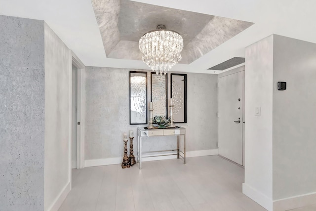 hallway with baseboards, an inviting chandelier, wood finished floors, and a raised ceiling