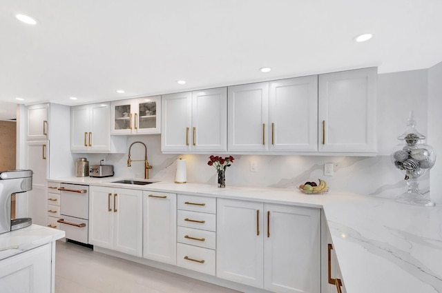 kitchen featuring dishwasher, a sink, light stone counters, glass insert cabinets, and recessed lighting