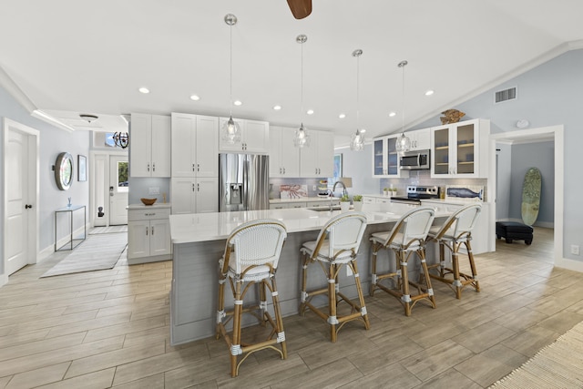 kitchen featuring stainless steel appliances, a sink, lofted ceiling, a spacious island, and light countertops