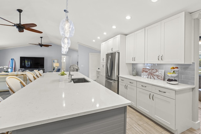 kitchen with a sink, stainless steel fridge, ceiling fan, decorative backsplash, and light wood-style flooring