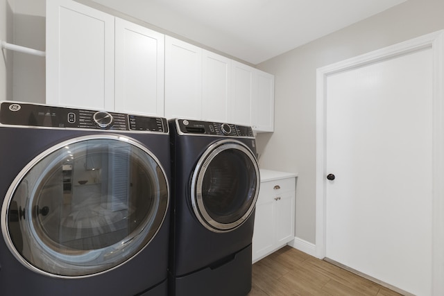 clothes washing area with washing machine and clothes dryer, cabinet space, light wood-style floors, and baseboards