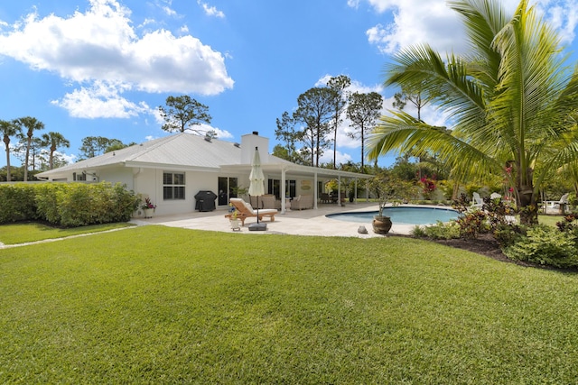 back of property featuring a patio, a yard, a chimney, and an outdoor pool