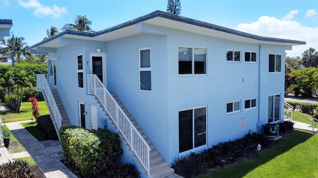 view of side of home with a lawn, central AC unit, stucco siding, and stairway