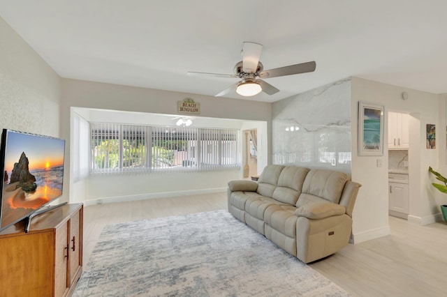 living area featuring light wood-style floors, baseboards, and ceiling fan