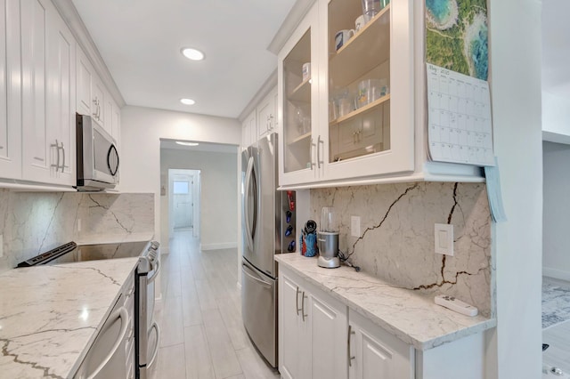 kitchen featuring backsplash, appliances with stainless steel finishes, baseboards, white cabinets, and light stone counters