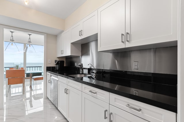 kitchen with dark countertops, dishwasher, a sink, white cabinets, and marble finish floor