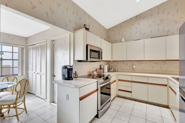 kitchen with appliances with stainless steel finishes, light countertops, wallpapered walls, light tile patterned floors, and vaulted ceiling