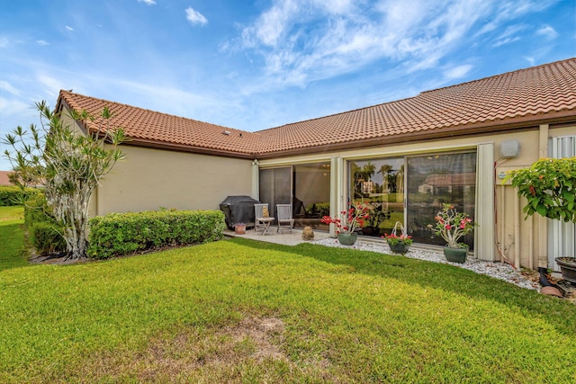 rear view of house with a tiled roof, a lawn, and stucco siding