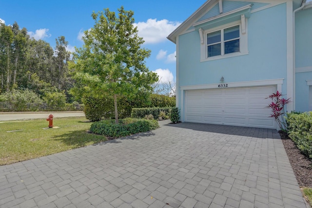 exterior space with a lawn, an attached garage, and decorative driveway