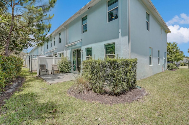 back of house featuring a lawn, fence, a patio, and stucco siding