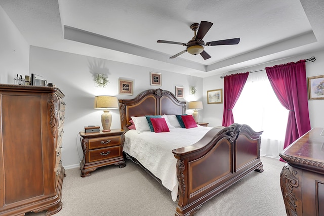 bedroom with light colored carpet, a raised ceiling, ceiling fan, and baseboards