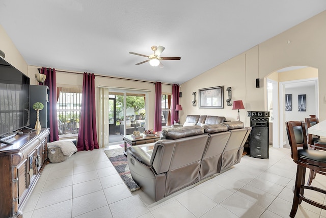living area featuring arched walkways, a ceiling fan, light tile patterned floors, and vaulted ceiling
