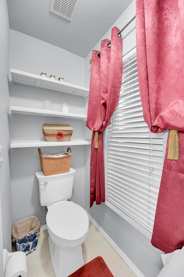 bathroom featuring a textured ceiling, visible vents, tile patterned floors, baseboards, and toilet