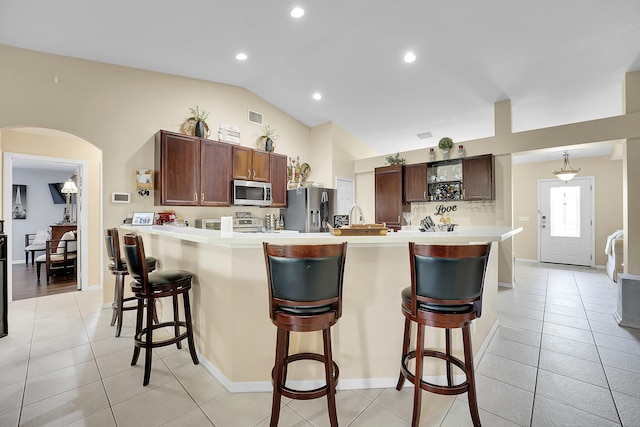 kitchen with a breakfast bar, arched walkways, stainless steel appliances, a peninsula, and light tile patterned floors
