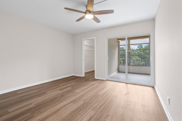 unfurnished bedroom featuring wood finished floors, a ceiling fan, a closet, baseboards, and a spacious closet