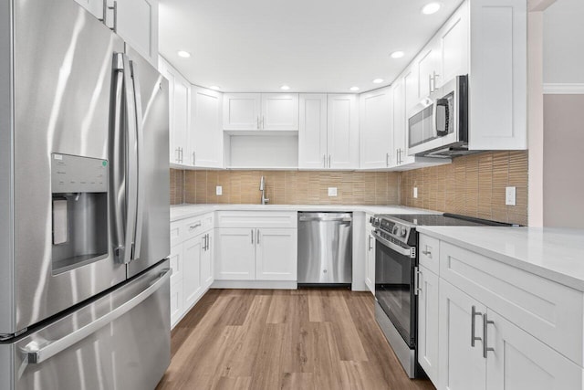 kitchen with a sink, white cabinets, light wood-type flooring, light countertops, and appliances with stainless steel finishes