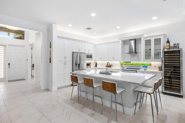 kitchen with wall chimney range hood, a breakfast bar area, a sink, wine cooler, and stainless steel appliances