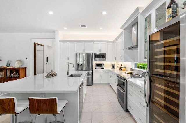 kitchen featuring marble finish floor, a kitchen bar, wall chimney exhaust hood, a sink, and appliances with stainless steel finishes