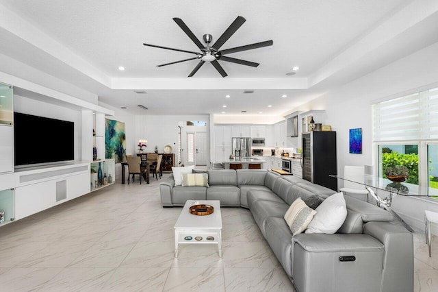 living area with recessed lighting, a ceiling fan, and a tray ceiling