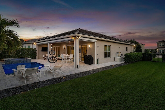 back of house featuring a pool with connected hot tub, fence, a yard, a patio, and stucco siding