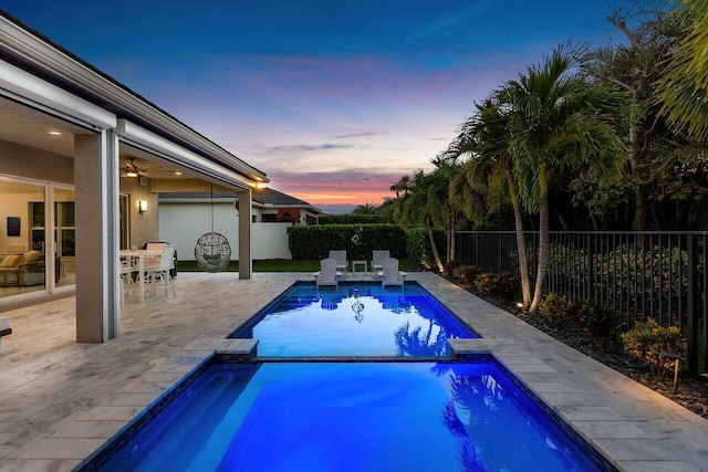 pool at dusk with outdoor dining area, a fenced backyard, a patio area, and a pool with connected hot tub
