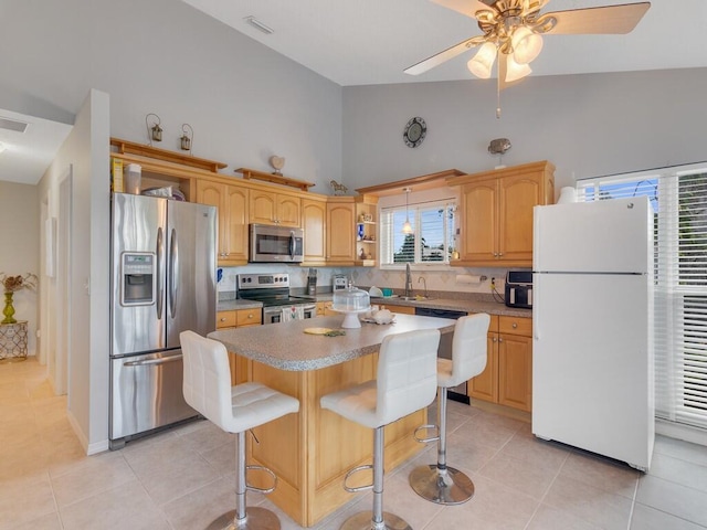 kitchen with a ceiling fan, a kitchen island, a sink, light tile patterned floors, and stainless steel appliances