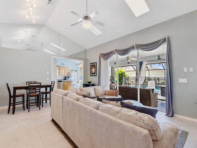 living area featuring baseboards, ceiling fan, vaulted ceiling with skylight, rail lighting, and light tile patterned floors