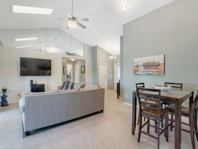living area featuring high vaulted ceiling, a skylight, light tile patterned floors, and ceiling fan with notable chandelier