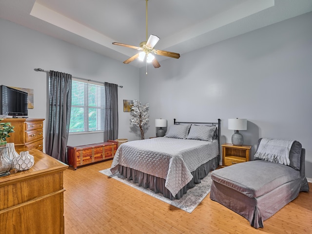 bedroom featuring a ceiling fan, light wood finished floors, and a tray ceiling