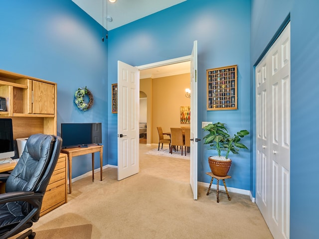 home office with arched walkways, baseboards, light carpet, and a high ceiling