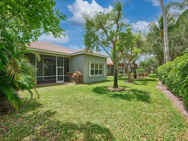 rear view of property with a lawn, stucco siding, a sunroom, and a tiled roof
