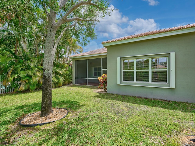 rear view of house featuring a lawn, stucco siding, and a sunroom