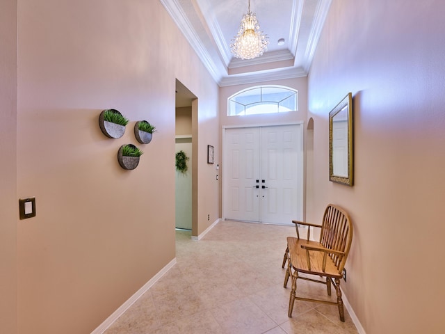 foyer featuring crown molding, baseboards, a raised ceiling, arched walkways, and a notable chandelier
