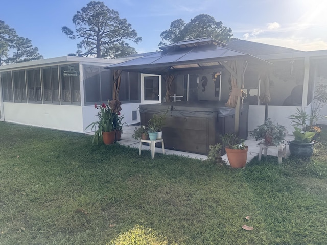 back of house with a hot tub, a lawn, a gazebo, and a sunroom