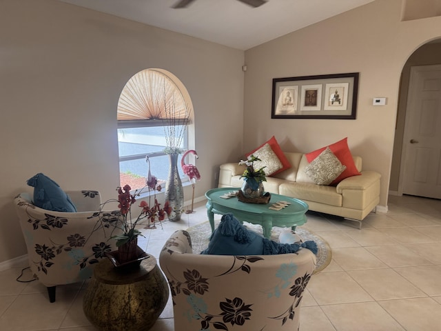 living room featuring light tile patterned floors, arched walkways, baseboards, and vaulted ceiling
