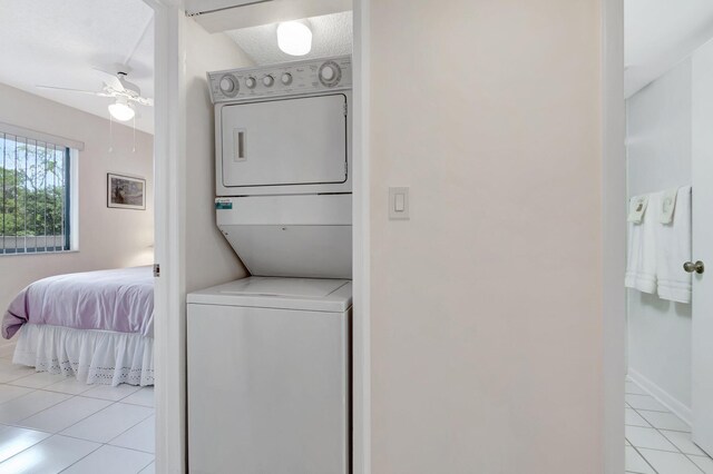 clothes washing area featuring tile patterned flooring, stacked washer and clothes dryer, laundry area, baseboards, and a ceiling fan