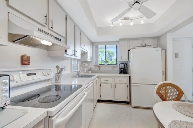 kitchen featuring white appliances, light countertops, under cabinet range hood, a tray ceiling, and a sink