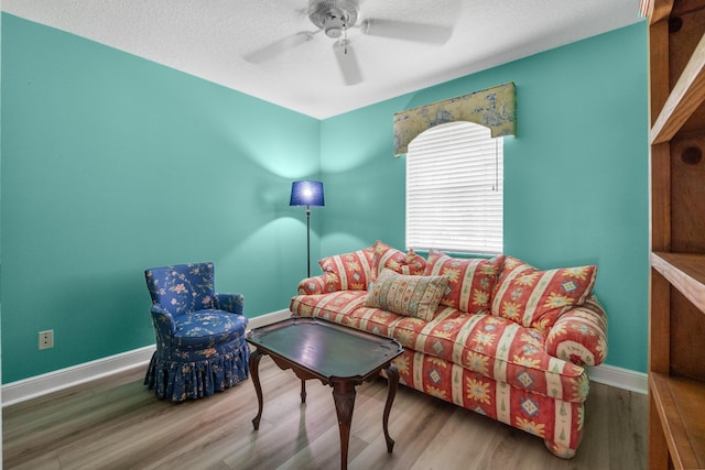 living area featuring wood finished floors, a ceiling fan, baseboards, and a textured ceiling