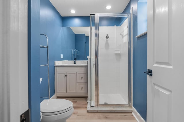 full bathroom with a stall shower, wood finished floors, vanity, toilet, and recessed lighting