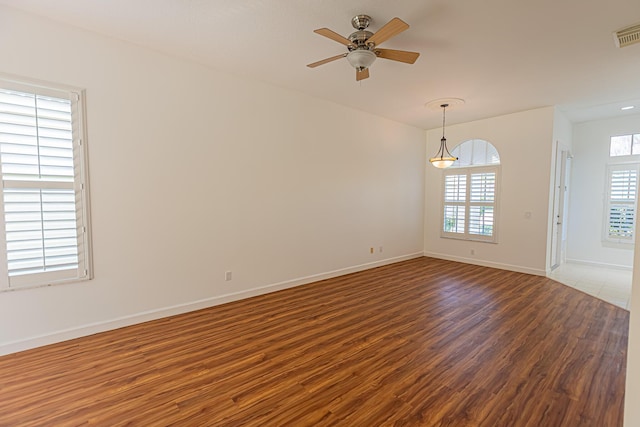 unfurnished room featuring baseboards, visible vents, a ceiling fan, and wood finished floors
