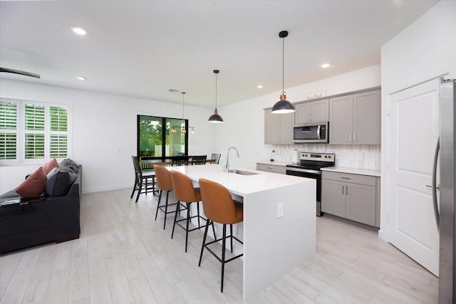 kitchen with light wood-type flooring, gray cabinets, appliances with stainless steel finishes, and a kitchen breakfast bar