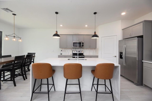 kitchen featuring appliances with stainless steel finishes, a sink, light countertops, gray cabinets, and backsplash